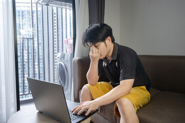 Stressed asian businessman sitting on a sofa at home and working on a laptop. tired man work from Home concept.