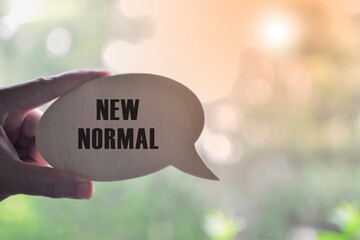 Hand holding black speech bubble with text NEW NORMAL with sunlight effect.