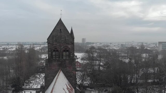 Panning drone view of 129 year old English church covered in snow with the town in background