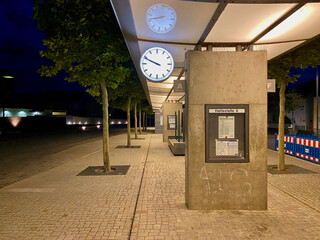 Moderner Bahnhof mit Betonwand und analoger runder leuchtender Uhr in der Nacht