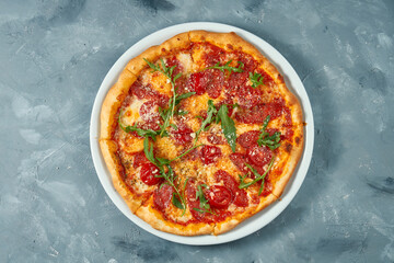 Italian pizza with salami, arugula and parmesan on a white plate. Concrete background. Top view