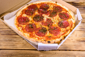 Pizza with salami sausage and parmesan cheese in cardboard box on a wooden table