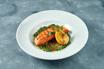 Grilled salmon steak with stewed spinach in white plate on concrete background