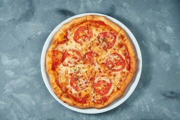 Classic italian pizza margarita with tomatoes and cheese in a white plate on a concrete background