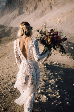 Anonymous female in beautiful lace dress with hand-tied flower bouquet walking on sand road