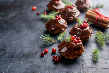 Christmas chocolate cupcakes, with icing, are decorated with a sprig of spruce, and cranberries. On a dark table dessert, with cinnamon sticks, snowflakes, serpentine.