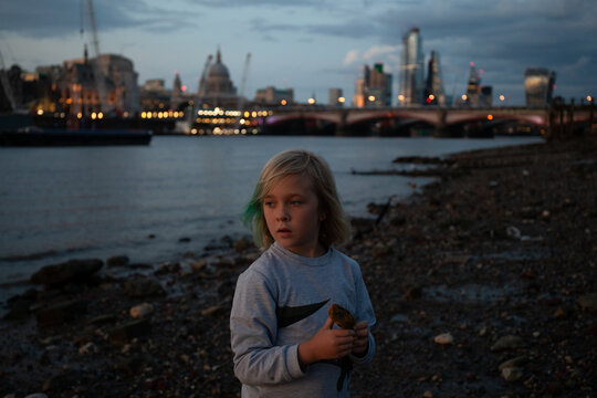 Child carrying a stone as she explores the south bank of the Thames at dusk.