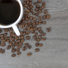 Grains of coffee with a cup of coffee on a wood background.