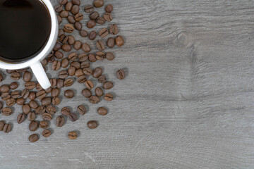 Grains of coffee with a cup of coffee on a wood background.