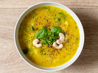 Hot vegan yellow curry soup with healthy vegetables and green salad in a white bowl top down view with bright wooden texture background