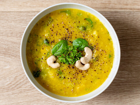 Hot Vegan Yellow Curry Soup With Healthy Vegetables And Green Salad In A White Bowl Top Down View With Bright Wooden Texture Background