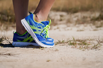 Close up view of a young woman standing on a natural dirt road in sports shoes getting ready to run and exercise