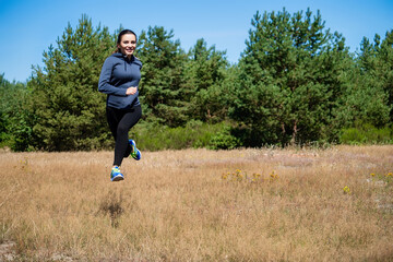 Young woman running on a natural meadow in the background of green trees and blue sky