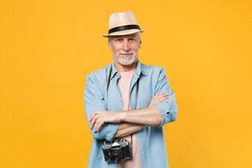 Smiling traveler tourist elderly gray-haired man in hat photo camera isolated on yellow background. Passenger traveling abroad on weekends getaway. Air flight journey concept. Holding hands crossed.