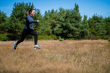 Young woman running on a natural meadow in the background of green trees and blue sky