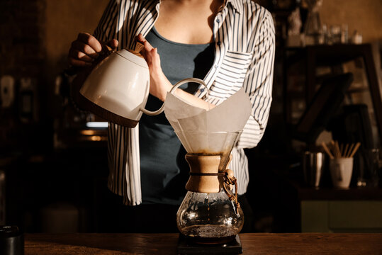 Female professional barista pouring hot water from kettle in chemex