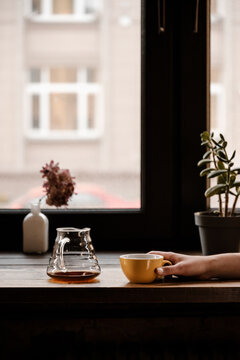 Close up of female hand holding yellow cup on table.
