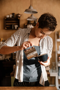 Female barista pouring milk from iron pitcher to cup.
