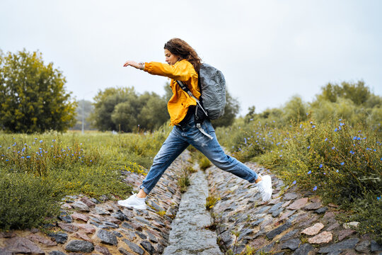 Young girl traveler jumps over a stream