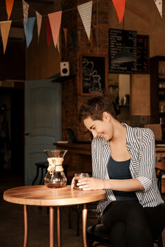 Beautiful smiling brunette girl drinking coffee from chemex.