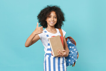 Smiling little african american kid schoolgirl 12-13 years old in striped clothes with backpack isolated on blue background studio. Childhood education in school concept. Hold books, showing thumb up.