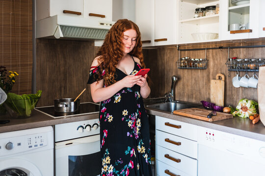 red haired woman standing in the kitchen using her phone