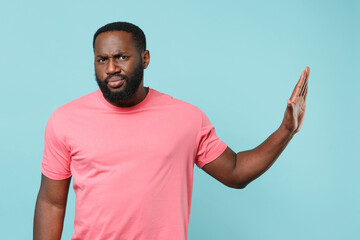 Displeased young african american man guy in casual pink t-shirt isolated on pastel blue background studio portrait. People lifestyle concept. Mock up copy space. Showing stop gesture with palm aside.