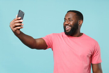 Smiling young african american man guy in casual pink t-shirt isolated on pastel blue wall background studio portrait. People lifestyle concept. Mock up copy space. Doing selfie shot on mobile phone.