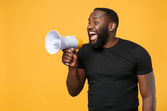 Cheerful african american man in casual black t-shirt isolated on yellow background studio portrait. People sincere emotions lifestyle concept. Mock up copy space. Scream in megaphone, looking aside.