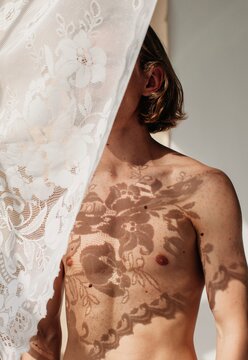 Sensual topless man looking in window with sheer curtain covering face