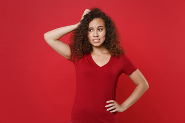 Preoccupied young african american woman girl in casual t-shirt posing isolated on red wall background studio portrait. People lifestyle concept. Mock up copy space. Put hand on head, looking aside.