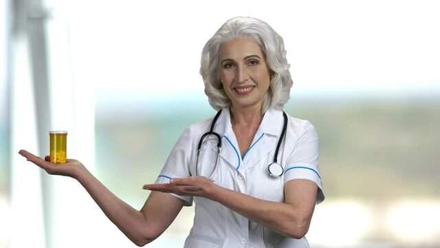 Female doctor presenting new pills. Smiling senior doctor showing unlabeled bottle of pills and looking at camera.