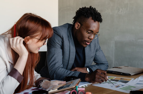 Concentrated multiethnic coworkers using tablet while discussing project in conference room