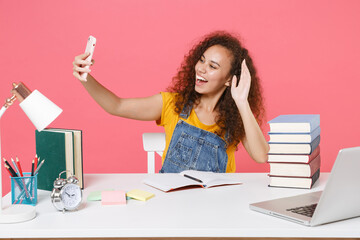 Funny african american girl in office isolated on pink background. Achievement business career. Education in school university college concept. Doing selfie shot on mobile phone, greeting with hand.