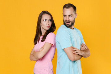 Fototapeta premium Side view of displeased couple friends guy girl in t-shirts isolated on yellow background. People lifestyle concept. Mock up copy space. Standing back to back hold hands crossed looking at each other.