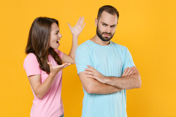 Displeased young couple friends guy girl in blue pink t-shirts posing isolated on yellow background studio portrait. People lifestyle concept. Mock up copy space. Screaming swearing spreading hands.