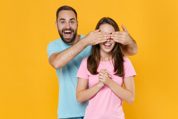 Cheerful excited young couple friends guy girl in blue pink t-shirts posing isolated on yellow wall background studio portrait. People lifestyle concept. Mock up copy space. Covering eyes with hands.