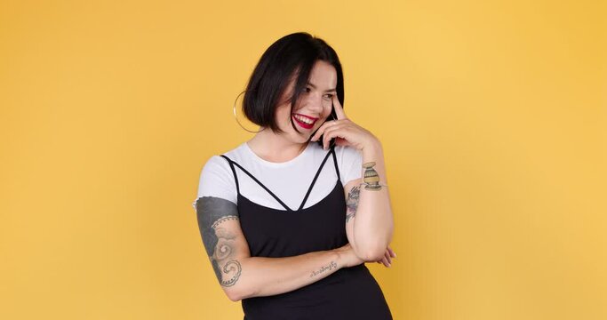 A young embarrassed woman with tattoo is listening compliments shy and laughing in yellow studio isolated. Portrait of shame female embarrassed smile. Shyness person expression.