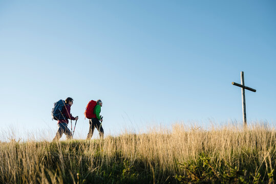 Couple of pilgrims close to a wooden cross walking along the hill in Saint James Way
