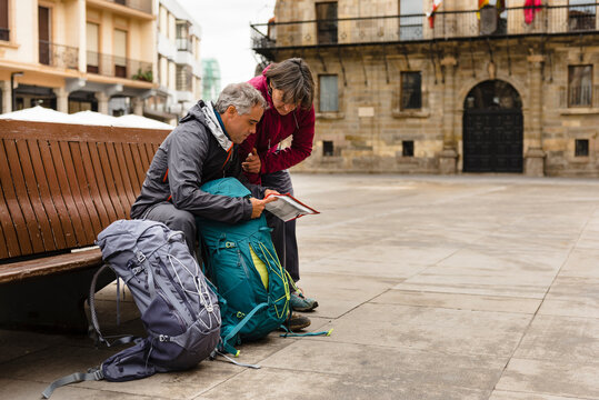 Couple of pilgrims seated in a bench reading a map in Astorga City on their way to Santiago de Compostela