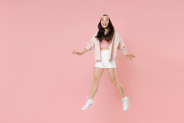 Fototapeta na wymiar Full length portrait excited young asian girl in casual clothes, cap isolated on pastel pink background studio portrait. People lifestyle concept. Mock up copy space. Jumping spreading hands and legs.