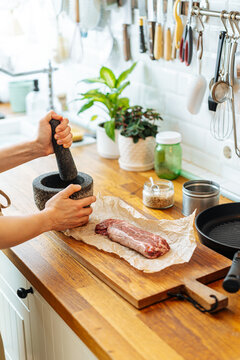 Person grinding spices in mortar on table with meat and utensil