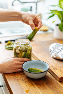 Person taking cucumbers from glass jar serving in bowl