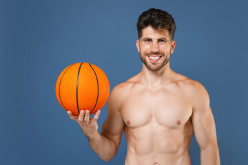 Smiling young fitness sporty strong guy bare-chested muscular sportsman basketball player isolated on blue wall background. Workout sport motivation lifestyle concept. Playing basketball hold ball.