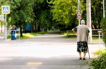 an elderly woman with a wand waits for the green light to cross the road