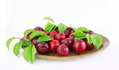 Fresh plums with leaves on a wooden plate close-up. Copy space