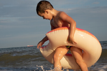 A cheerful boy 5 years old swims in the sea on an inflatable ring in the form of a donut on a sunny day.