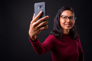 Portrait of happy young beautiful Asian businesswoman taking selfie