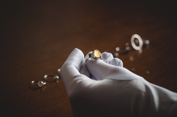 a jeweler examines a piece of jewelry in a white glove.