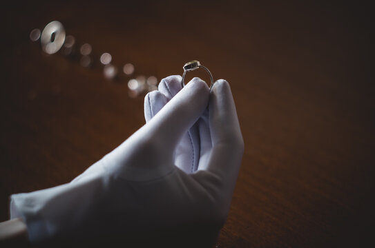 A Jeweler Examines A Piece Of Jewelry In A White Glove.